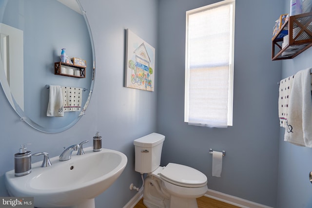 half bath with a sink, baseboards, toilet, and wood finished floors