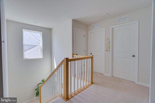 hallway with visible vents, carpet, baseboards, and an upstairs landing