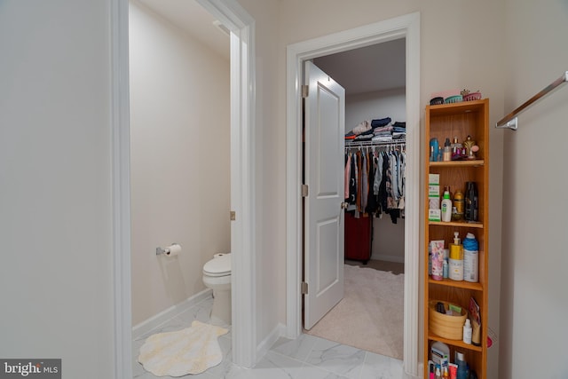 bathroom with baseboards, marble finish floor, a walk in closet, and toilet