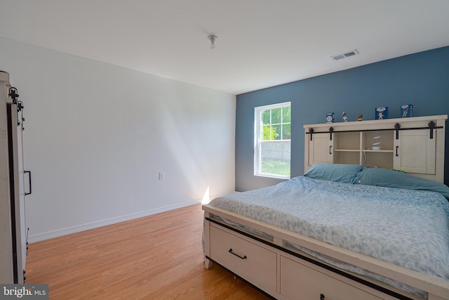 bedroom with light wood-style floors, a barn door, baseboards, and visible vents