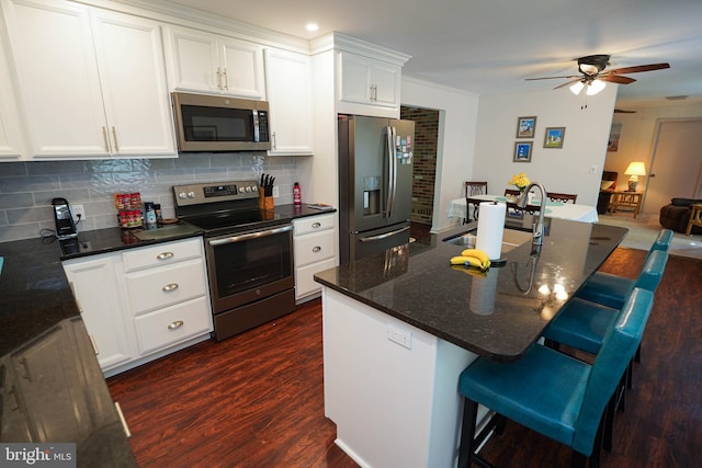 kitchen with dark wood-style flooring, stainless steel appliances, a ceiling fan, and a breakfast bar area