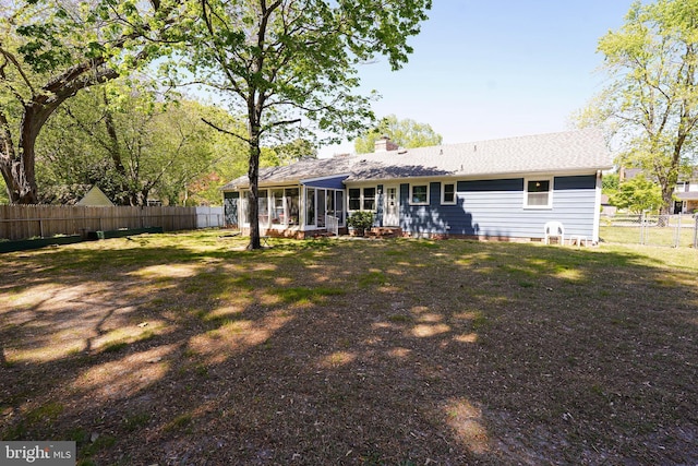 rear view of house with a fenced backyard, a chimney, and a sunroom