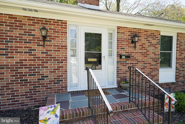 entrance to property featuring a chimney and brick siding