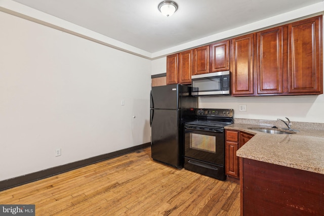 kitchen featuring a sink, light wood-type flooring, baseboards, black appliances, and light stone counters