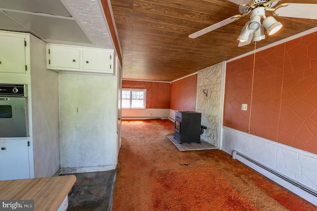 unfurnished living room with a ceiling fan, a wood stove, wood ceiling, a baseboard radiator, and carpet