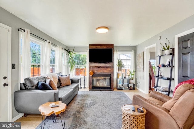 living area featuring a fireplace with flush hearth, baseboards, and light wood-style flooring