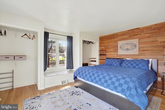 bedroom with visible vents, baseboards, wood finished floors, and wooden walls