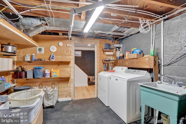 clothes washing area featuring laundry area, washer and dryer, wooden walls, a sink, and concrete block wall