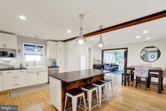 kitchen with white cabinets, dark countertops, appliances with stainless steel finishes, light wood-style floors, and tasteful backsplash
