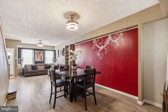 dining area featuring baseboards, a textured ceiling, and wood finished floors