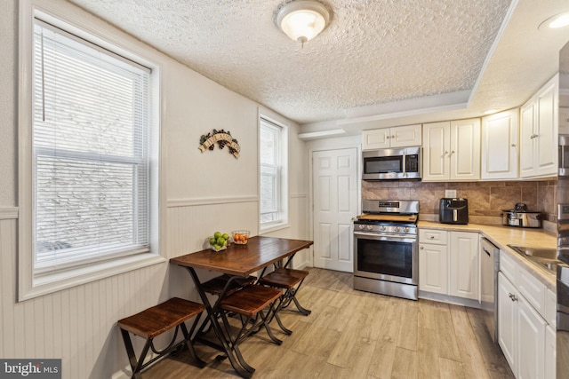 kitchen with appliances with stainless steel finishes, plenty of natural light, light wood-type flooring, and a textured ceiling