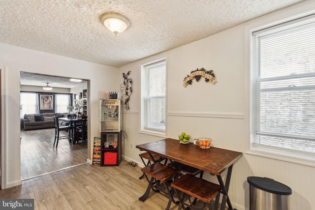 dining area with a wainscoted wall, light wood-style flooring, and a textured ceiling