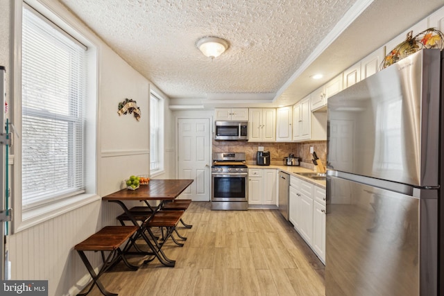 kitchen featuring light wood-style floors, light countertops, a textured ceiling, stainless steel appliances, and decorative backsplash