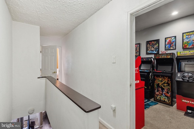 corridor featuring carpet floors, a textured ceiling, baseboards, and an upstairs landing