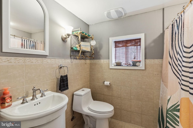 full bathroom with a sink, toilet, tile patterned floors, a wainscoted wall, and tile walls