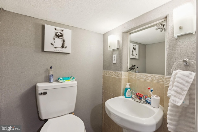 bathroom with tile walls, a sink, a wainscoted wall, toilet, and a textured wall