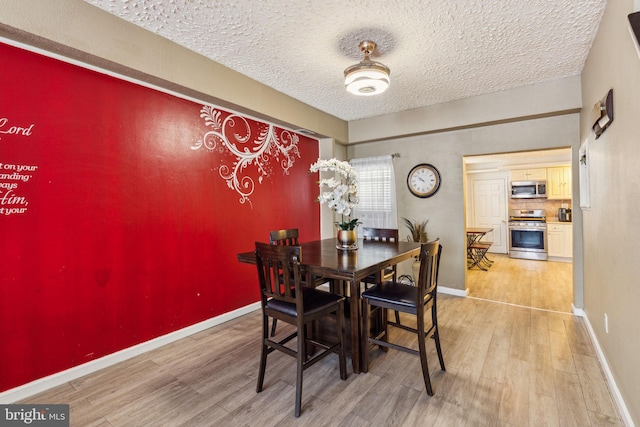 dining space with baseboards, a textured ceiling, and wood finished floors