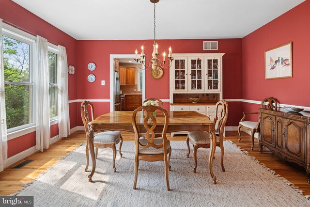 dining area featuring a notable chandelier, visible vents, a healthy amount of sunlight, and light wood-style flooring