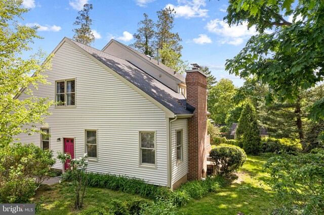 view of home's exterior featuring roof with shingles, a chimney, and a lawn