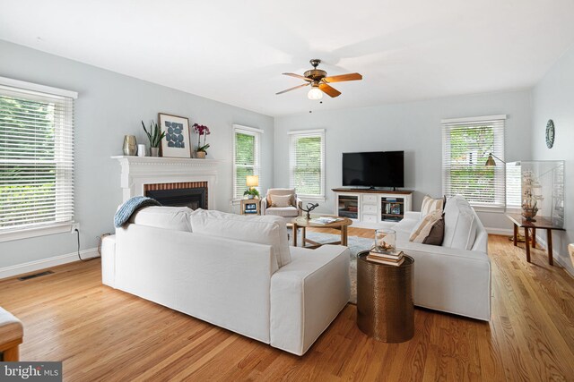 living room with visible vents, a fireplace, baseboards, light wood-style flooring, and a wealth of natural light