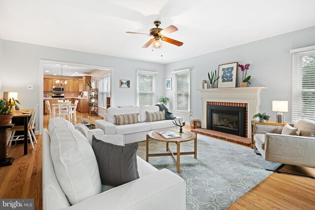 living area with light wood-style floors, plenty of natural light, a fireplace, and a ceiling fan