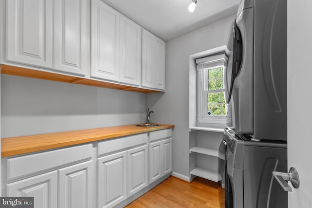 washroom with stacked washer and clothes dryer, baseboards, light wood-style flooring, a sink, and cabinet space