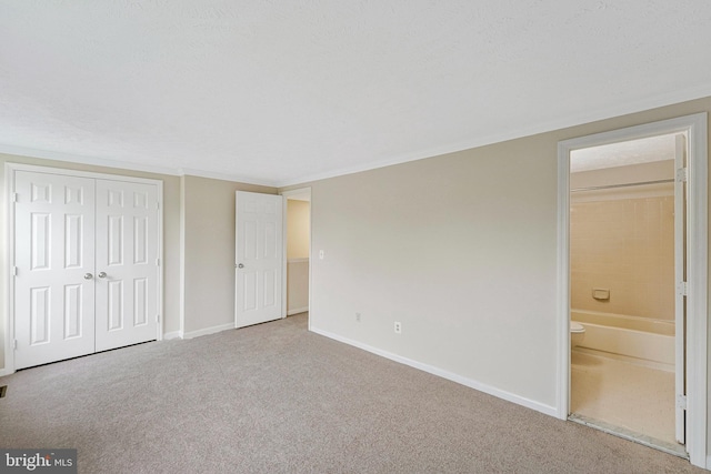 unfurnished bedroom with carpet flooring, a closet, baseboards, ensuite bathroom, and ornamental molding