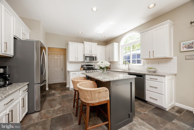 kitchen with stone finish flooring, appliances with stainless steel finishes, white cabinetry, and tasteful backsplash