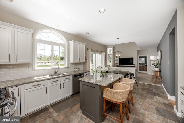kitchen with appliances with stainless steel finishes, a sink, stone finish floor, decorative backsplash, and a kitchen island