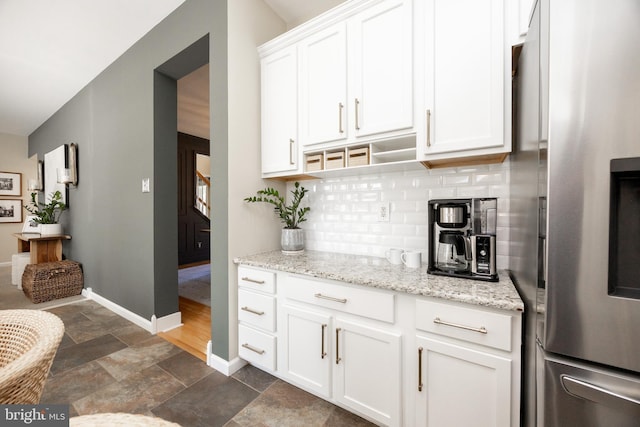 bar with stairs, baseboards, stainless steel refrigerator with ice dispenser, stone finish flooring, and backsplash