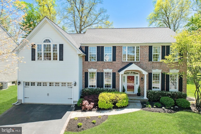 colonial inspired home with a garage, central AC, a front yard, and aphalt driveway