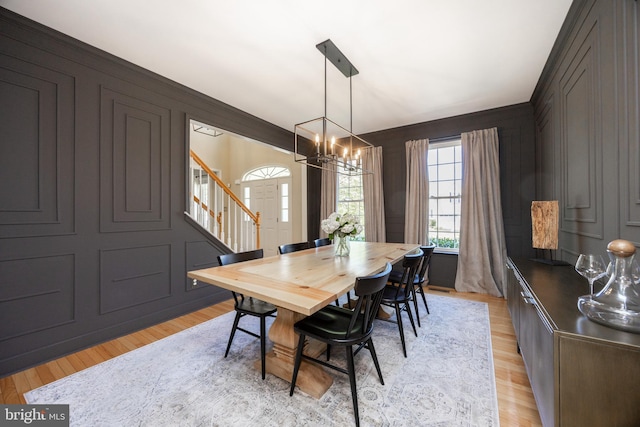 dining area with light wood-style floors, a decorative wall, a chandelier, and stairway
