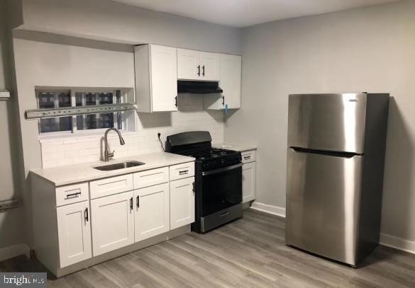 kitchen featuring a sink, light countertops, freestanding refrigerator, black range with gas cooktop, and under cabinet range hood