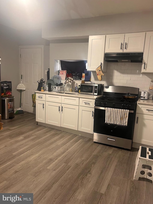 kitchen with under cabinet range hood, stainless steel appliances, white cabinets, and wood finished floors