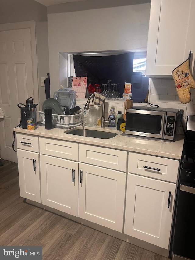 kitchen with a sink, range, white cabinetry, stainless steel microwave, and dark wood-type flooring