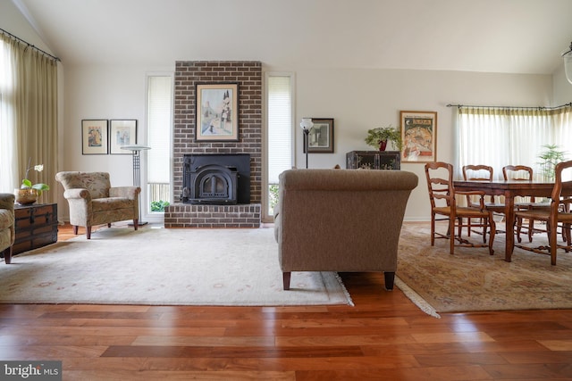 living area featuring plenty of natural light, a brick fireplace, wood finished floors, and vaulted ceiling
