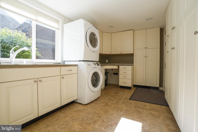 laundry room featuring stacked washing maching and dryer, a sink, cabinet space, and a wealth of natural light