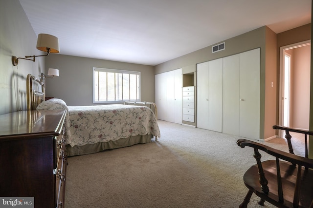 bedroom with light colored carpet, multiple closets, and visible vents