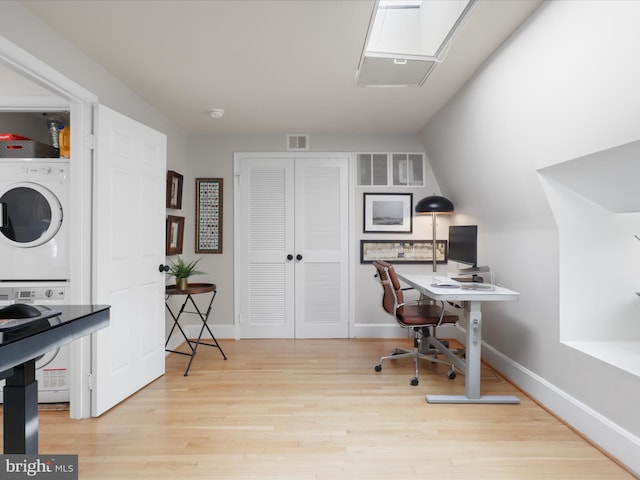 office space featuring visible vents, baseboards, wood finished floors, and stacked washer / dryer