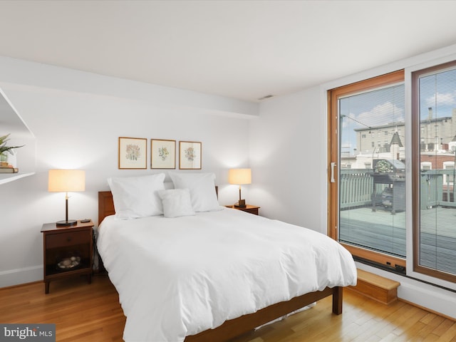 bedroom with baseboards, access to outside, wood finished floors, and visible vents