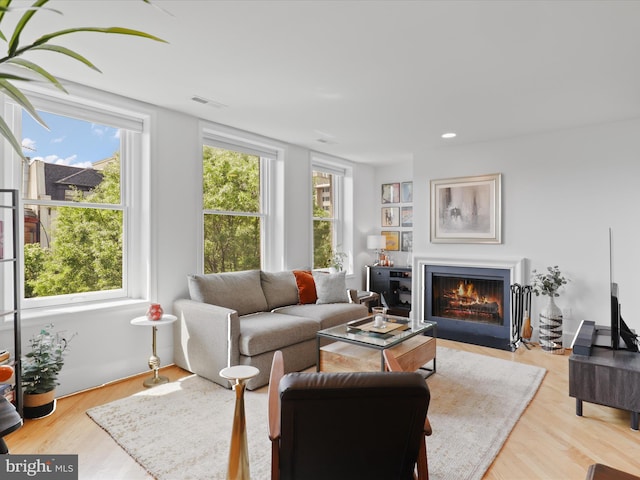living room with a fireplace with flush hearth, recessed lighting, wood finished floors, and visible vents