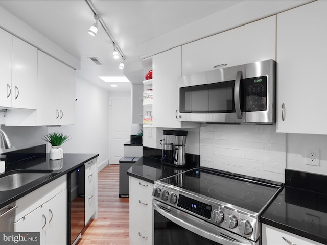 kitchen with white cabinets, appliances with stainless steel finishes, a sink, light wood-type flooring, and visible vents