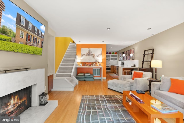 living room with a lit fireplace, wood finished floors, and stairway