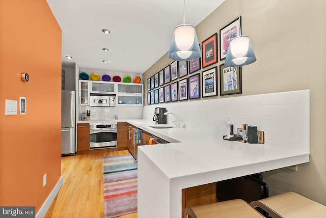kitchen featuring tasteful backsplash, a sink, a peninsula, light wood finished floors, and stainless steel appliances