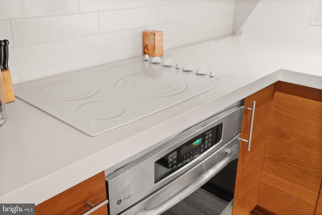 details with white electric cooktop, backsplash, and stainless steel oven
