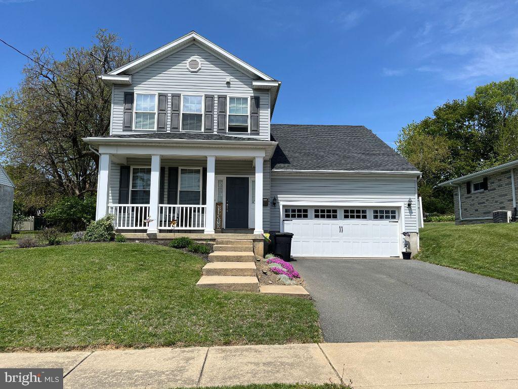 traditional home with covered porch, driveway, cooling unit, a front lawn, and an attached garage