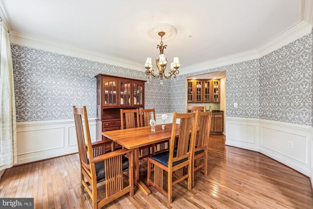 dining room featuring wallpapered walls, a chandelier, a wainscoted wall, ornamental molding, and light wood-style flooring