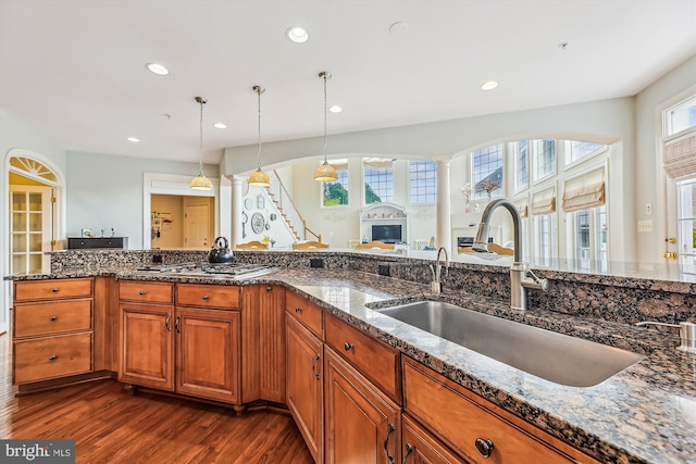 kitchen with a sink, dark wood-style floors, brown cabinetry, dark stone countertops, and recessed lighting