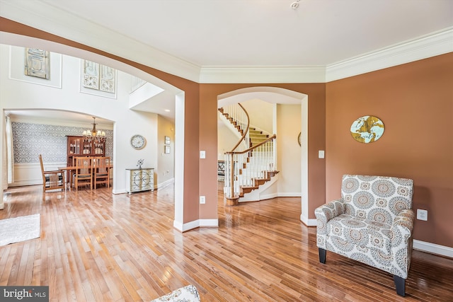 living area featuring arched walkways, light wood-style floors, stairs, and ornamental molding