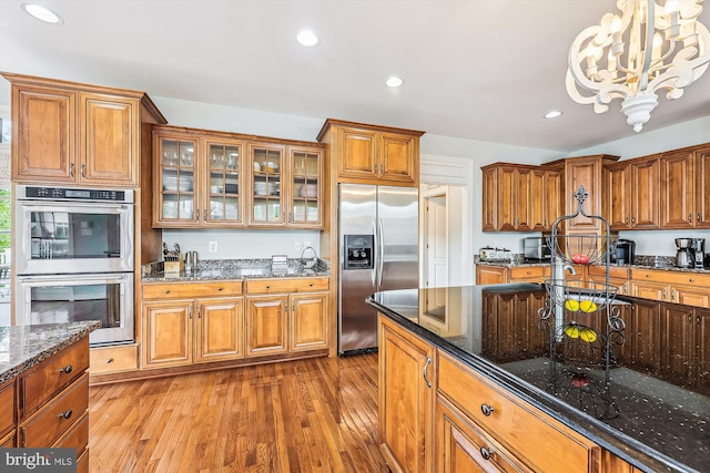 kitchen featuring appliances with stainless steel finishes, brown cabinets, hardwood / wood-style floors, a chandelier, and glass insert cabinets